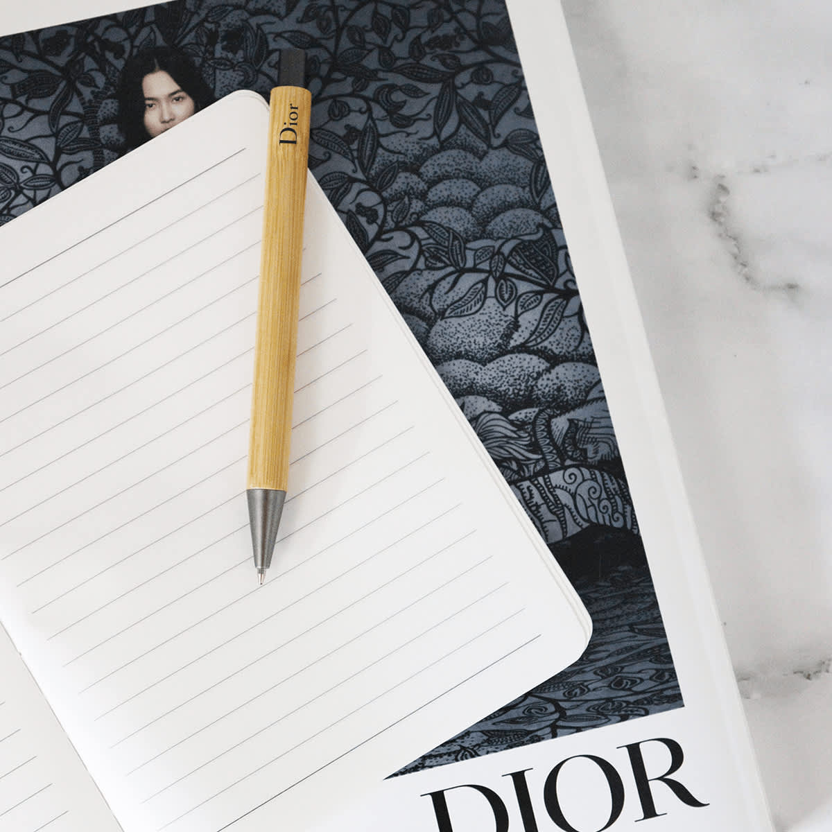 A bamboo pen with a metallic tip resting on a lined notebook, against a dark patterned background featuring a logo. Panda Pen - Image 1