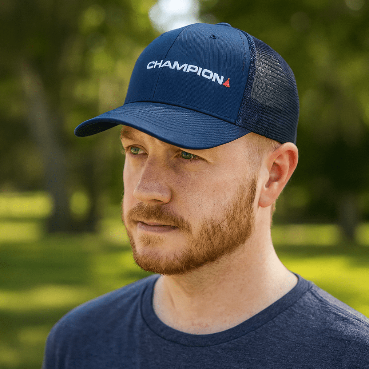 A navy snapback trucker cap with a mesh back and a logo, worn by a man with a beard in a natural setting. Snapback Truckers Cap - Image 1