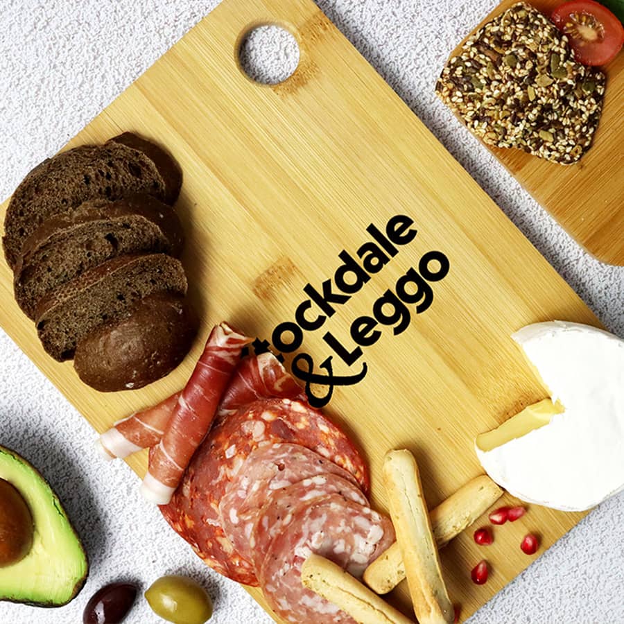 A large bamboo cutting board with assorted food items, including bread, meats, cheese, and an avocado, featuring a logo. Bamboo Cutting Board (Large) - Image 1