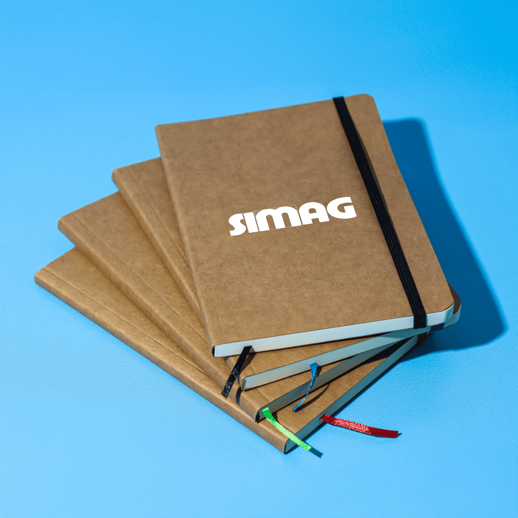 A stack of four brown notebooks with an elastic band closure, featuring a branded logo on the front cover. Jodha Notebook - Image 1