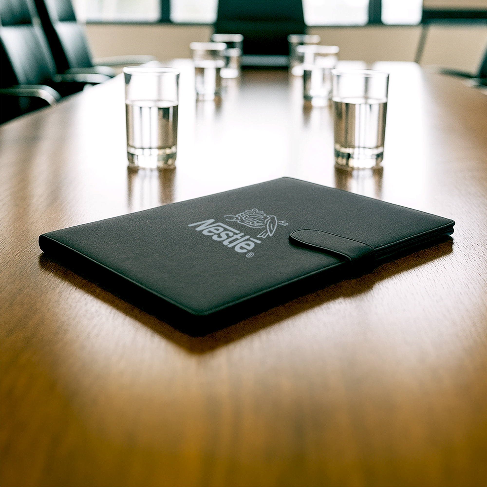 A black portfolio with a logo, resting on a wooden conference table, surrounded by glasses of water. The Original RPET Portfolio - Image 1