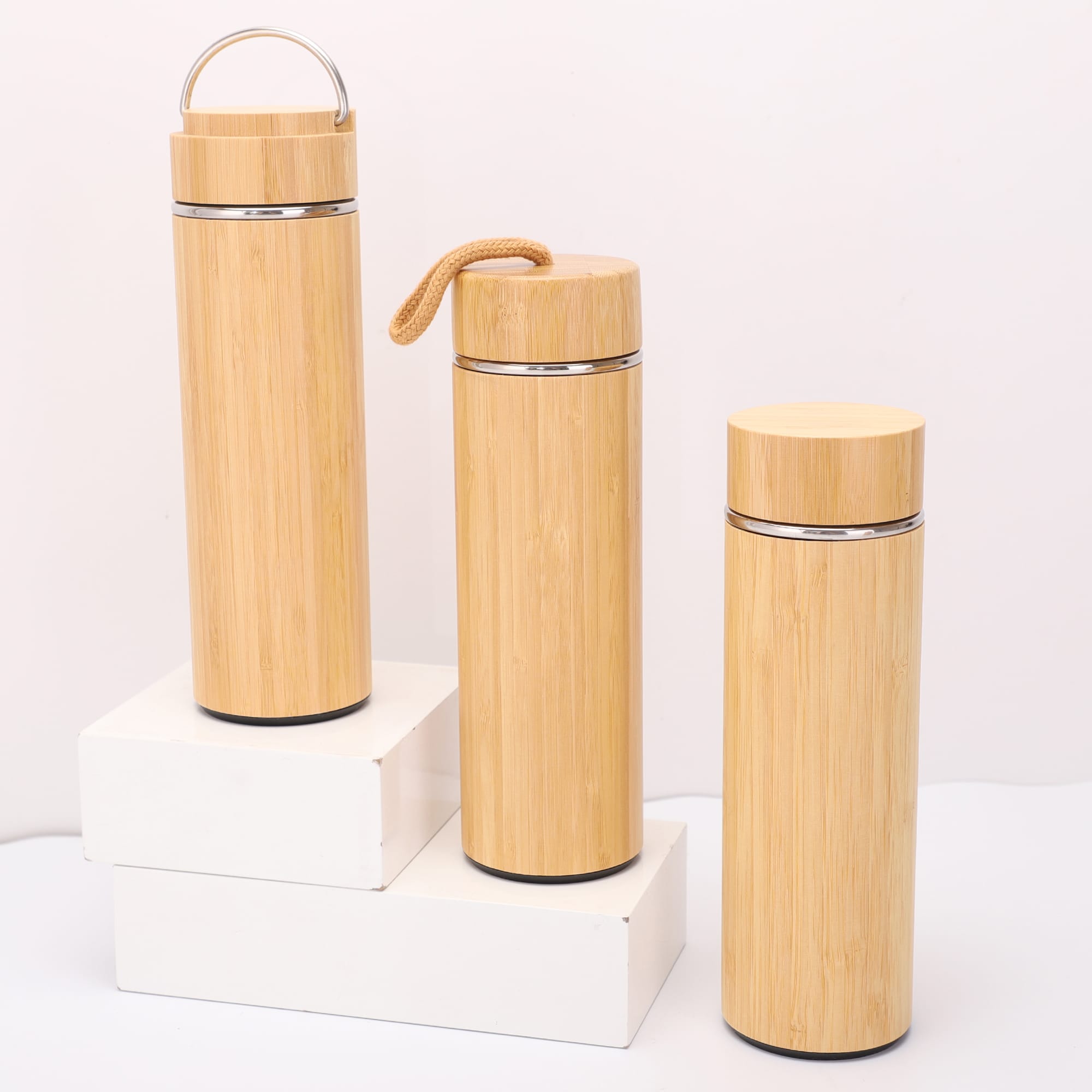 A drink bottle trio in natural bamboo finish, featuring metal accents and various styles, displayed on a white platform. Burra Bamboo Drink Bottle - Image 1