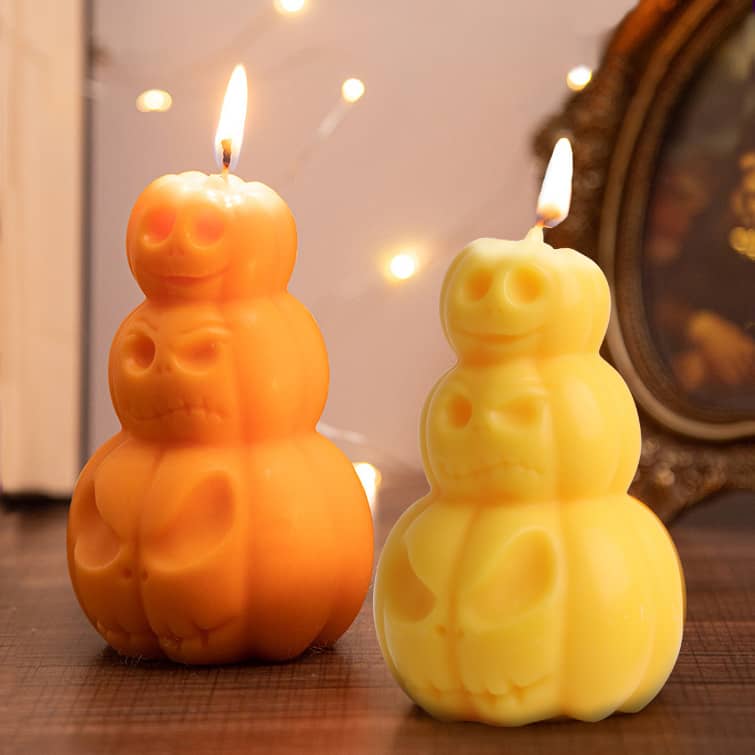 Triple pumpkin-shaped candles in orange and yellow, featuring carved skull designs, with flames flickering from the tops. Triple Pumpkin Shape Candles - Image 1