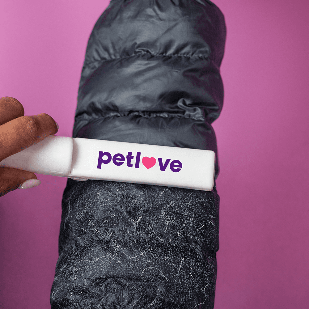 A lint remover in white with a logo, removing lint from a black puffer jacket against a pink background. Stick n Roll Lint Remover - Image 1