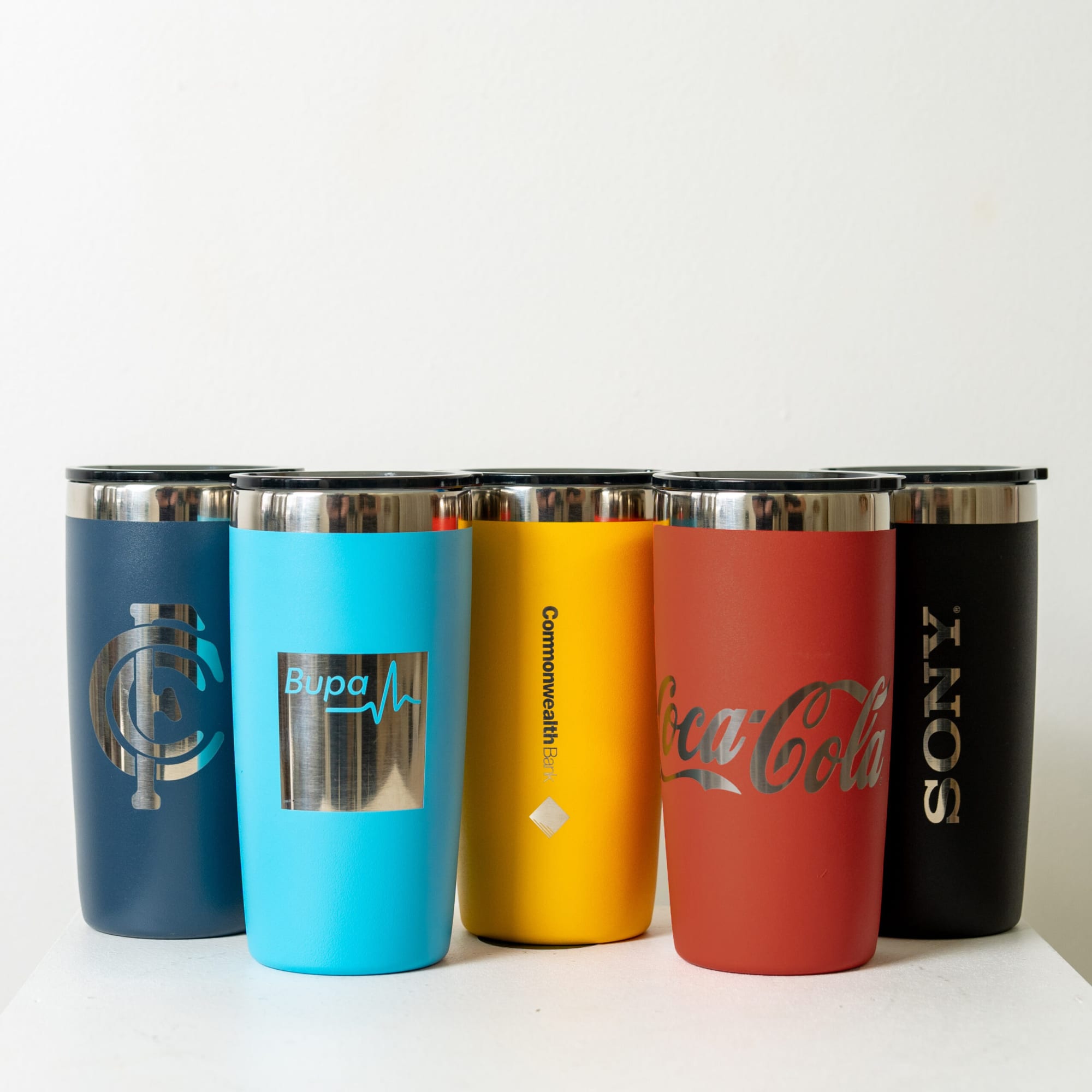 A drink tumbler set in various colours including navy, blue, yellow, red, and black, featuring logos on some. The Sanny Tumbler 320ml - Image 1