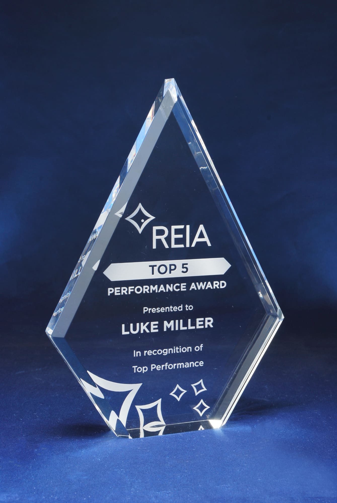 A diamond-shaped acrylic trophy with a clear finish and a blue background. Features engraving and a logo. Diamond Acrylic Trophy - Image 1