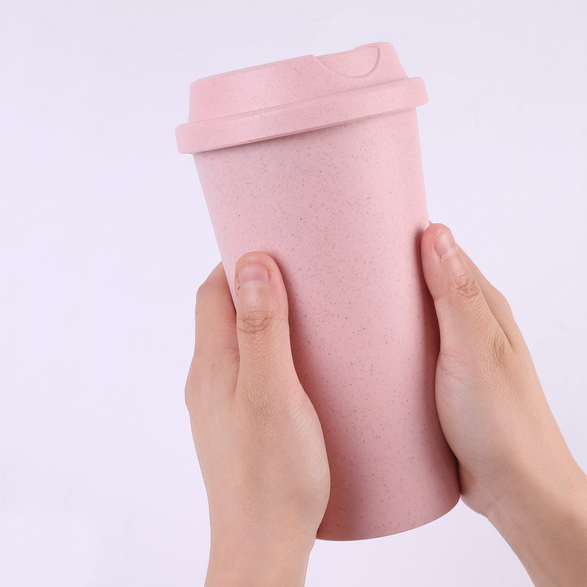 A reusable coffee cup in soft pink, being held in two hands, featuring a lid and a textured finish. Fresh Bamboo Cup - Image 1