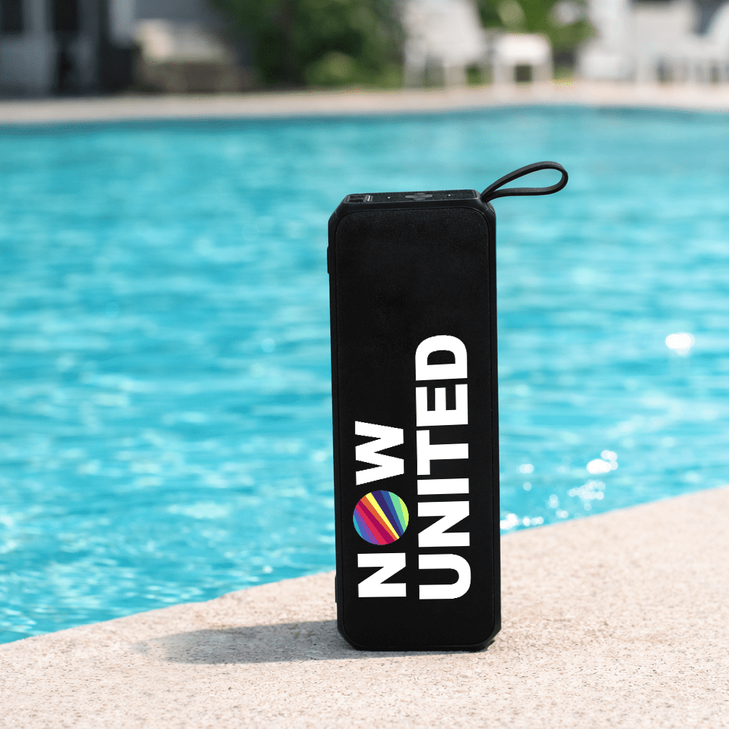 A black portable speaker with a round logo, sitting by a blue pool. Sunrise Solar Speaker - Image 1