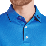 A close-up of a men's blue polo shirt featuring a tonal dot print and a logo on the collar.