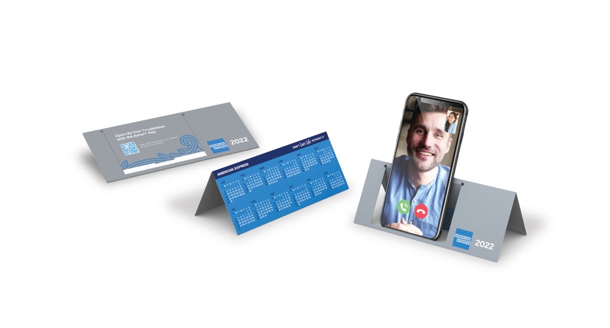 A foldable phone stand in grey, featuring a calendar design on one side and a smartphone propped up on the other. Fold Up Phone Stand - Image 1