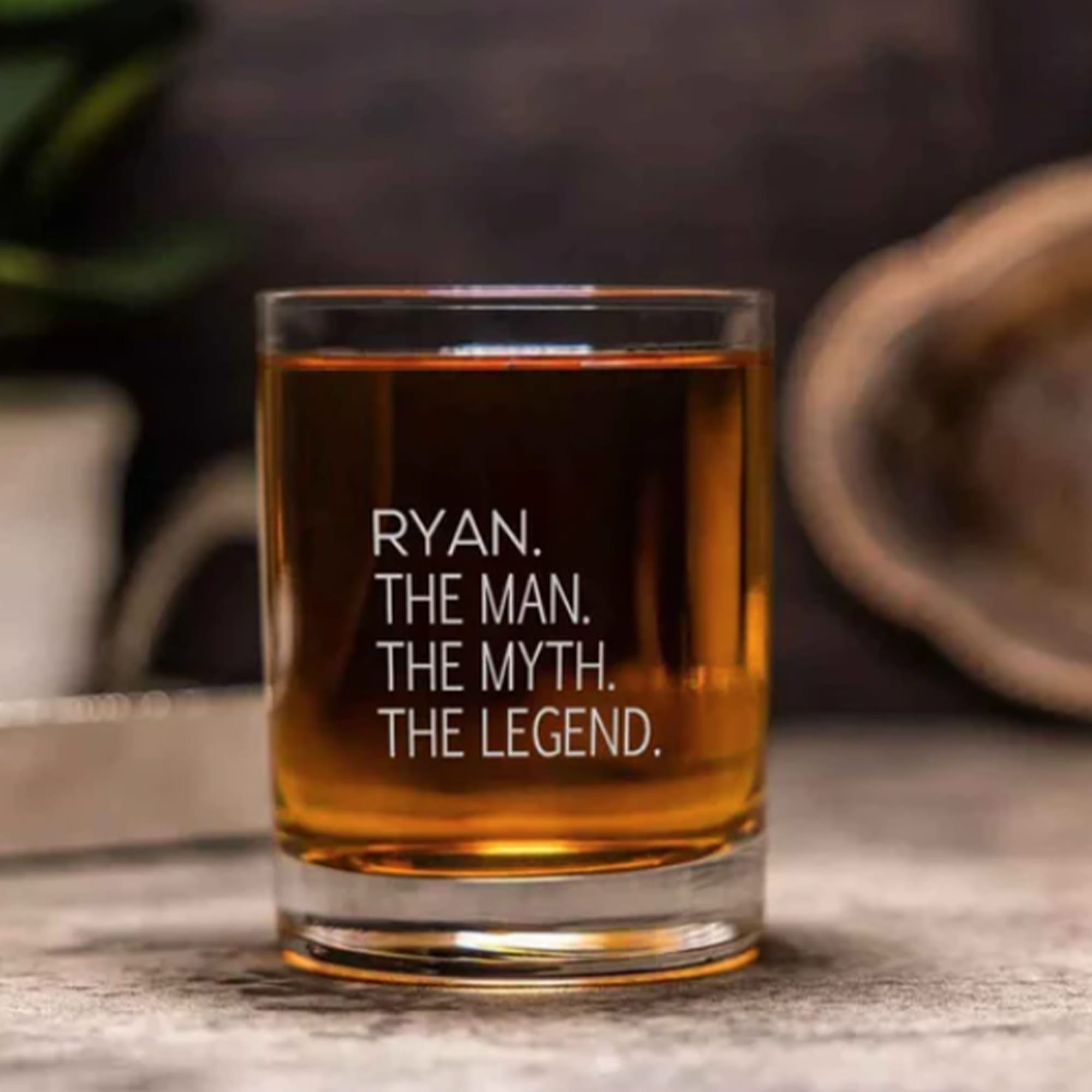 A glass tumbler filled with amber liquid, featuring a clear branding logo, set on a wooden surface. Oakland Glass Tumbler 210ml - Image 1