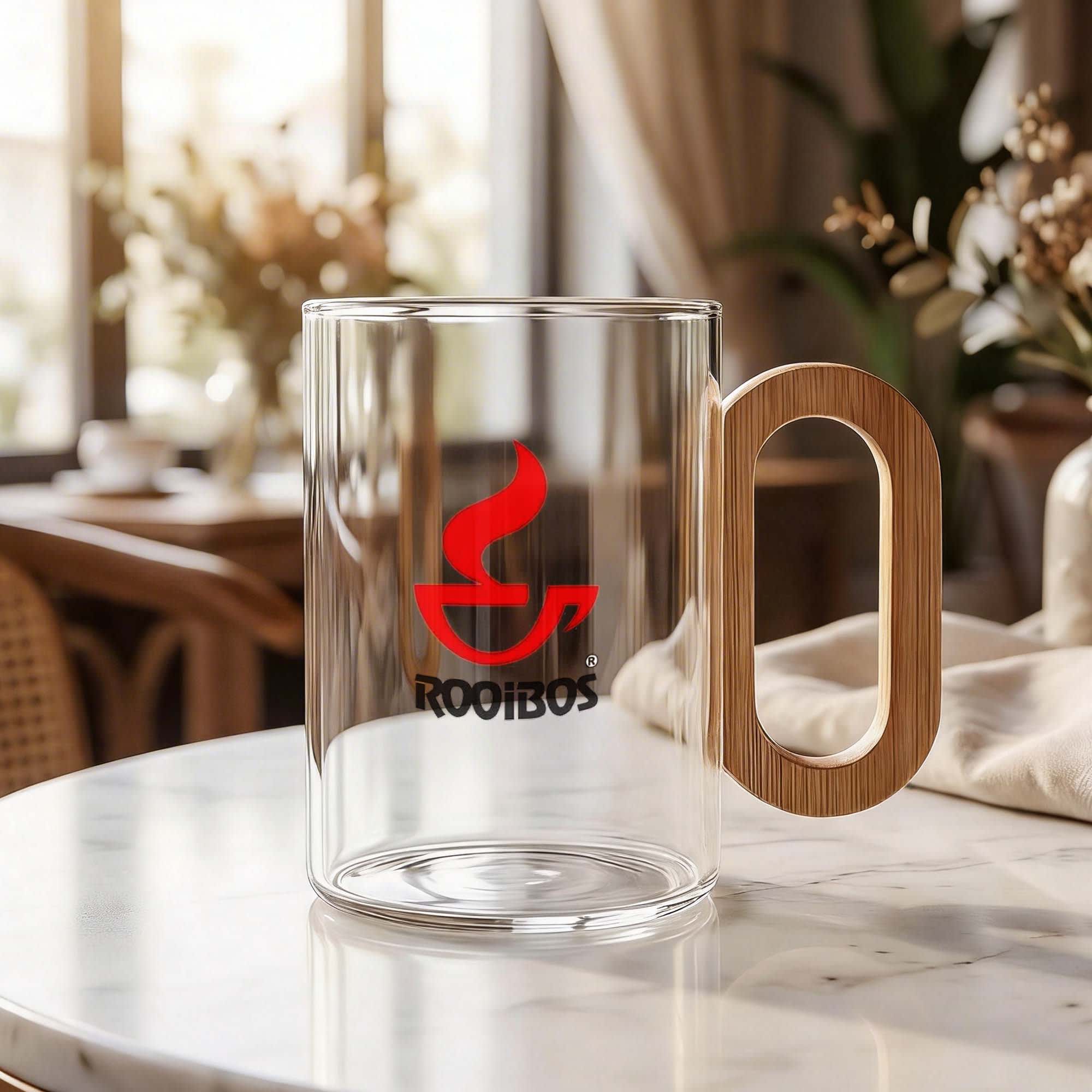A clear glass coffee cup with a bamboo handle and a logo, set on a marble table with a cozy background. Villa Glass Coffee Cup - Image 1