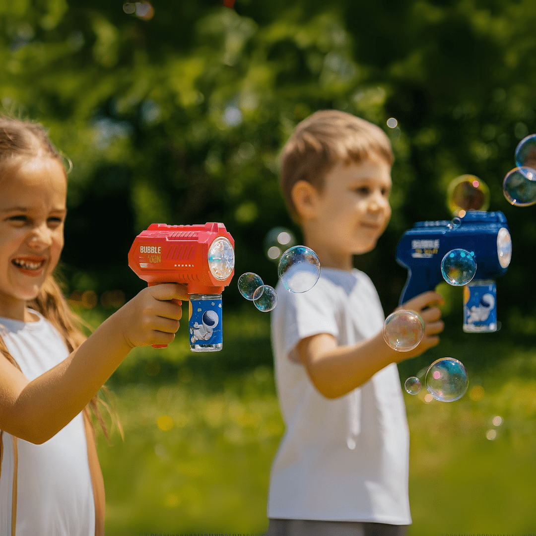 A red and a blue bubble gun are held by children, creating bubbles against a blurred green backdrop. Bubble '07 Bubble Gun - Image 1