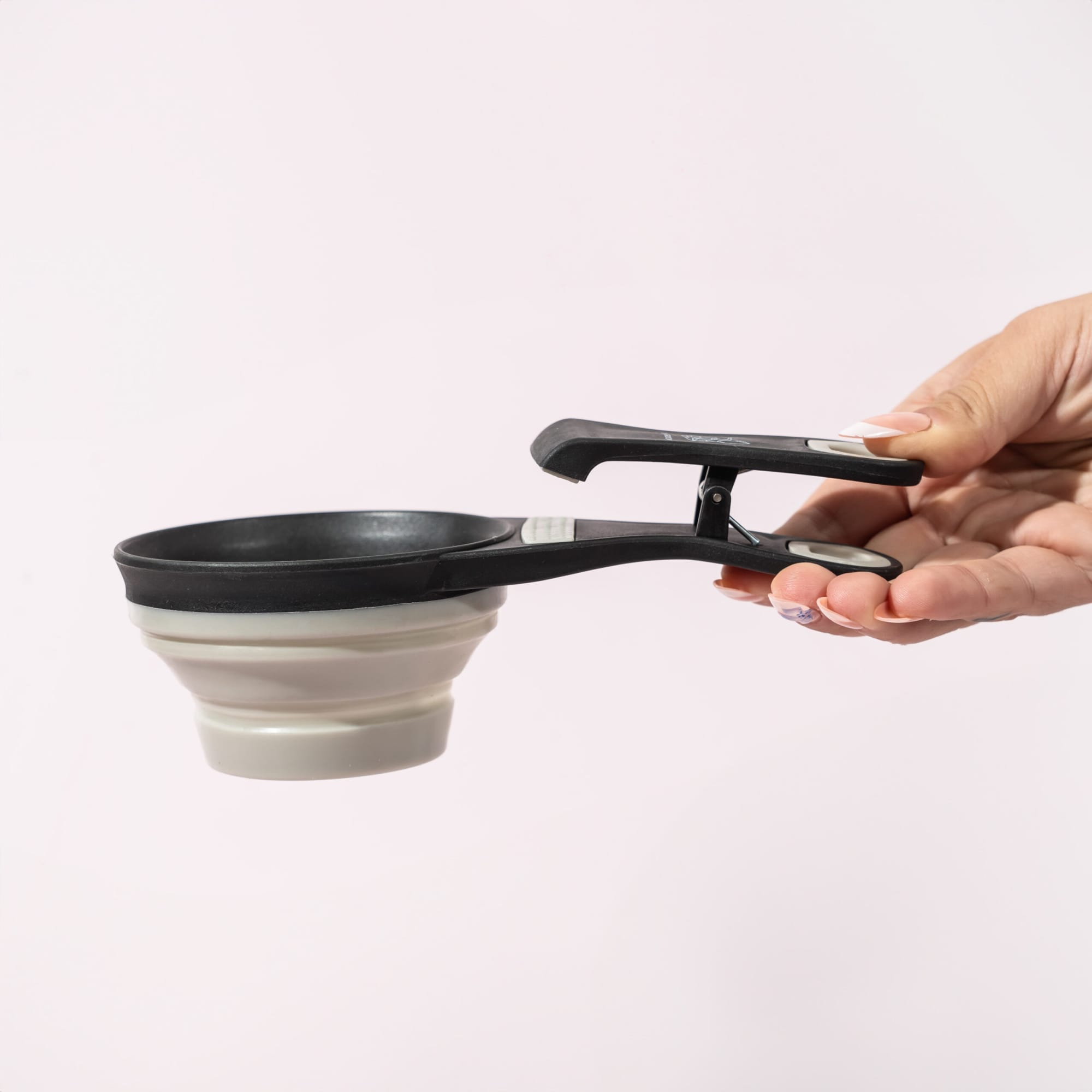 A collapsible silicone pet food scoop and bag clip in black and grey, held by a hand against a light background. Collapsible Silicone Pet Food Scoop & Bag Clip - Image 1