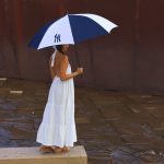 A navy and white umbrella with a logo, held by a person in a white dress, standing on a stone surface.