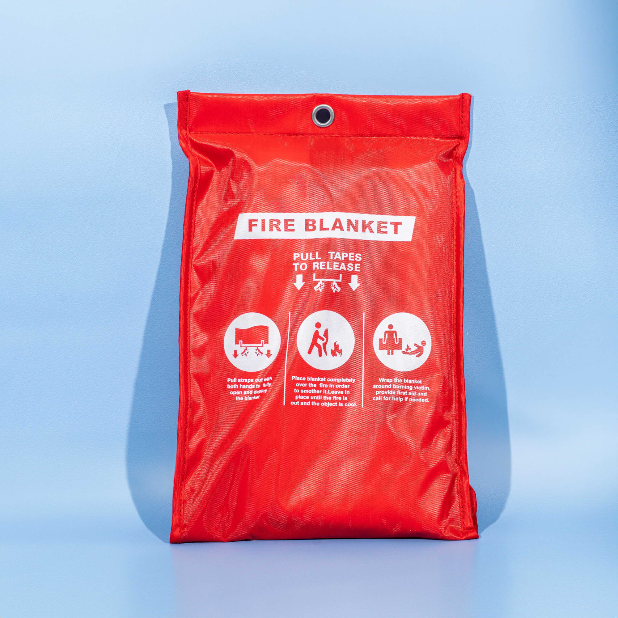 A red fire blanket in a protective bag featuring a logo and illustrated instructions for use. Fiberglass Emergency Fire Blanket - Image 1