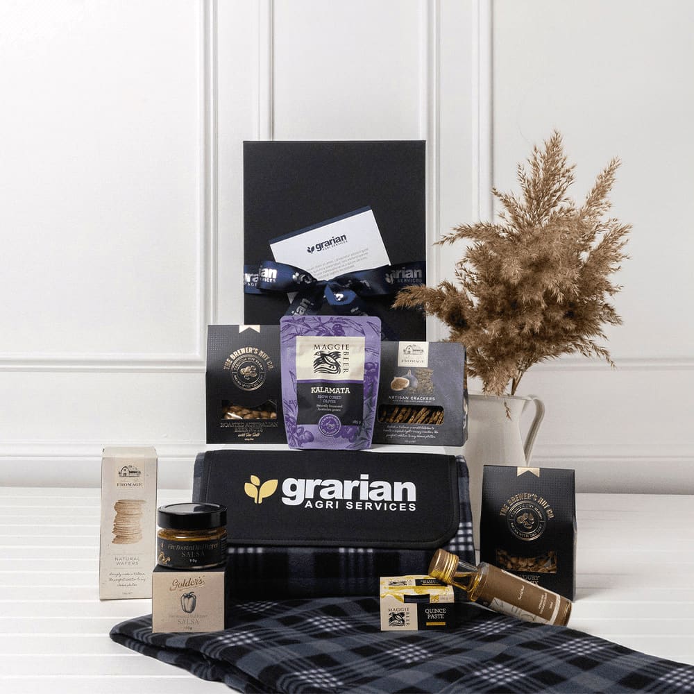 A picnic gift pack featuring a drink bottle, gourmet snacks, honey, and a checkered blanket in blue and black tones. The Branded Gourmet Picnic Gift Pack - Image 1