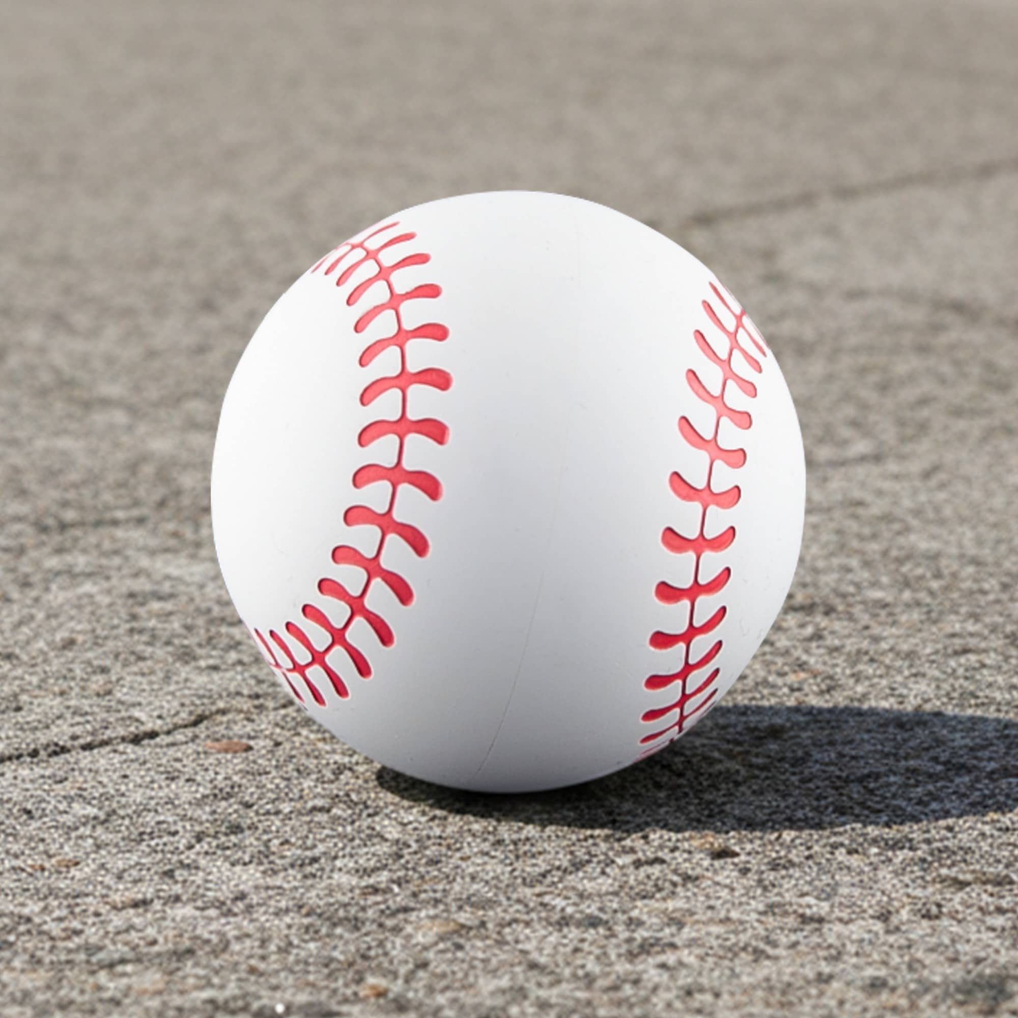 A high bounce baseball in white with red stitching, resting on a grey surface. The product has a logo. High Bounce Base Ball - Image 1