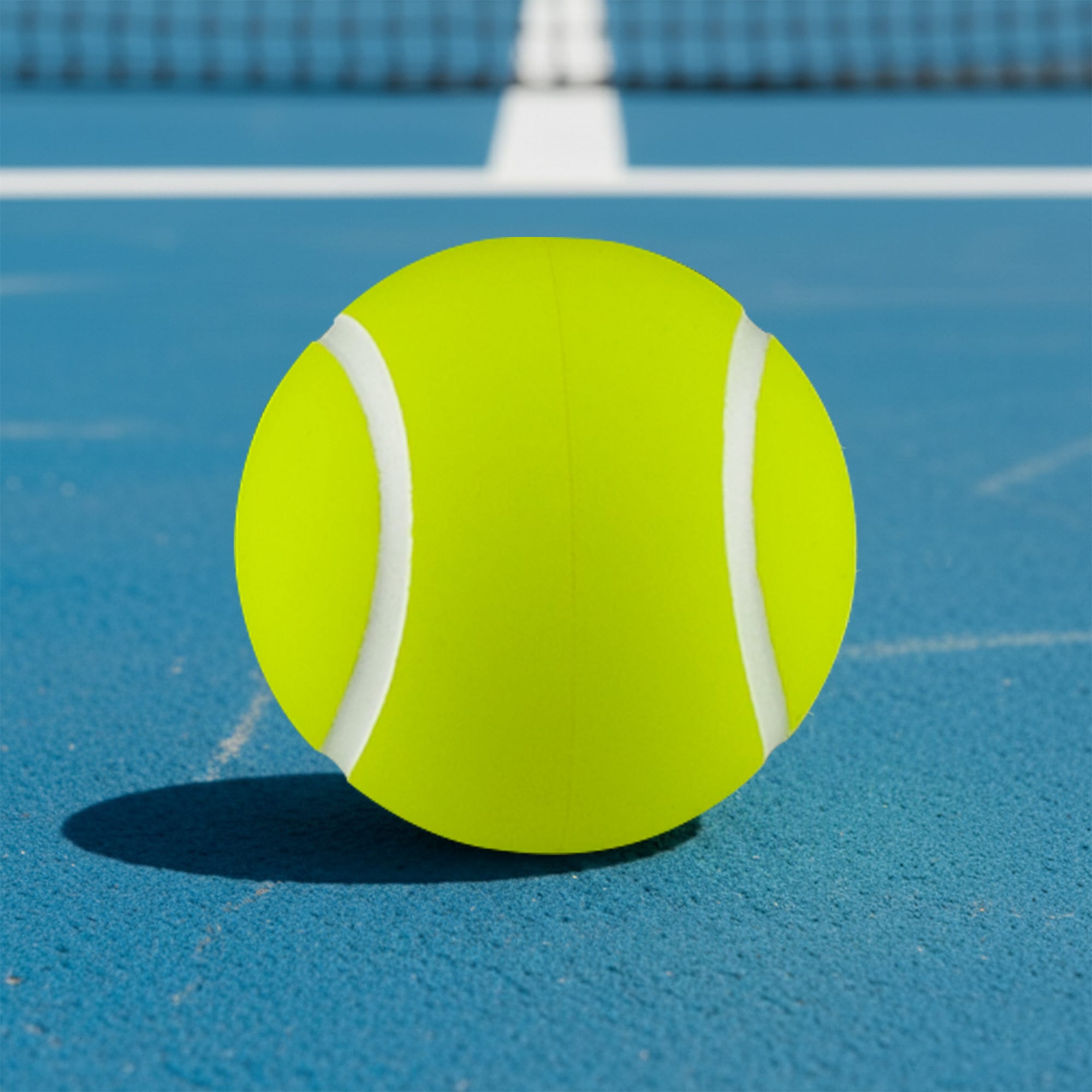 A bright yellow tennis ball sits on a blue court, featuring white stripes and a smooth texture. High Bounce Tennis Ball - Image 1