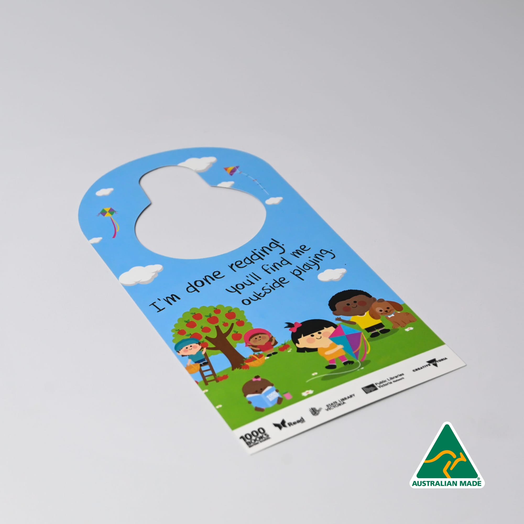 A door hanger featuring a colourful design with children playing outside, set against a blue background and greenery. Door Hanger - Image 1