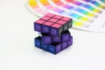 A Rubik's Cube 3x3 in black, purple, and blue featuring designs on the squares, alongside a colour palette guide.
