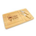 A bamboo cheese board with two metal knives, featuring a logo and a carved area for serving.