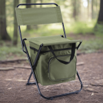 A green foldable camping chair with a cooler bag attached, set on a forest floor. It features a zippered cooler compartment.