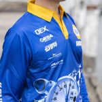 A blue and yellow long sleeve fishing polo featuring a logo and a dynamic sublimated design.