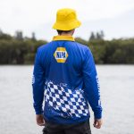 A blue long sleeve polyester fishing polo featuring a checkered pattern and a logo. A yellow bucket hat is worn.
