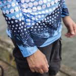 A long sleeve fishing tee featuring a blue and white dot pattern and abstract design, with a visible logo.