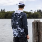 A men's polyester sublimated 1/4 zip fishing hoodie in navy and grey, featuring a hood and a logo, worn by a person by the water.