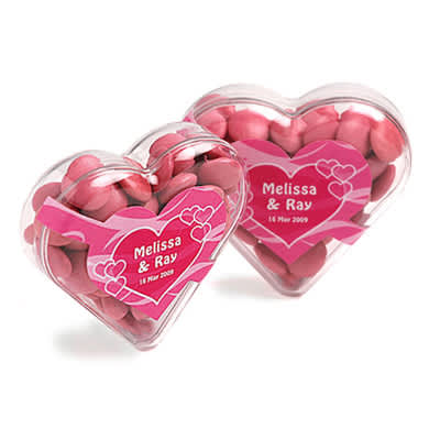 Acrylic heart container filled with pink chocolate beans, featuring a decorative heart-shaped design and a logo. Acrylic Heart with Choc Beans 50g - Image 1