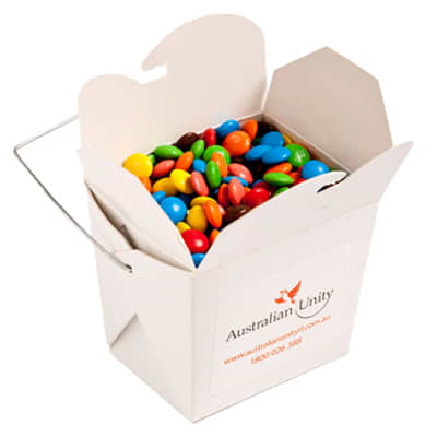 A white cardboard noodle box filled with colourful M&Ms, featuring a metal wire handle. White Cardboard Noodle Box with Mini M&Ms 100g - Image 1