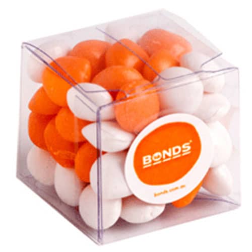 A cube-shaped container filled with orange and white chewy fruit candies. The container has a branding logo on it. Cube with Chewy Fruits 60g - Image 1