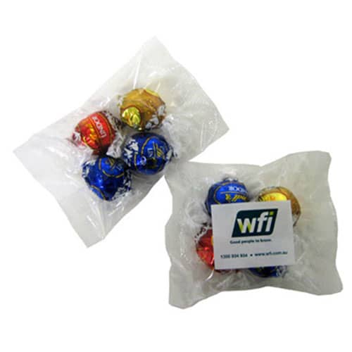 Four wrapped chocolate truffles in red, gold, blue, and silver packaging, presented in two plastic bags. Lindor Balls x4 - Image 1