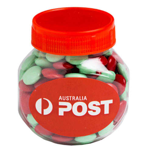 A clear plastic jar filled with red and green chocolate beans, featuring an orange lid and a logo. Plastic Jar filled with CHRISTMAS Choc Beans 170g - Image 1