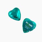 A teal chocolate heart wrapped in foil, featuring a circular branding label on one side.