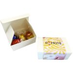 A white box containing four assorted chocolate balls in shiny red, gold, and blue wrappers.