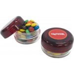 A small red screw cap jar filled with colourful M&Ms, featuring a logo on the lid.