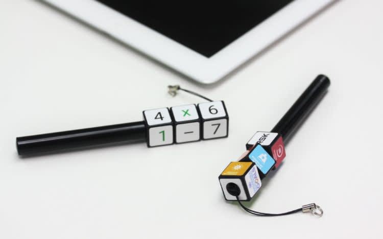 Two black plastic pens with colourful cube designs attached, resting beside a tablet device. Rubik's Pen - Image 1
