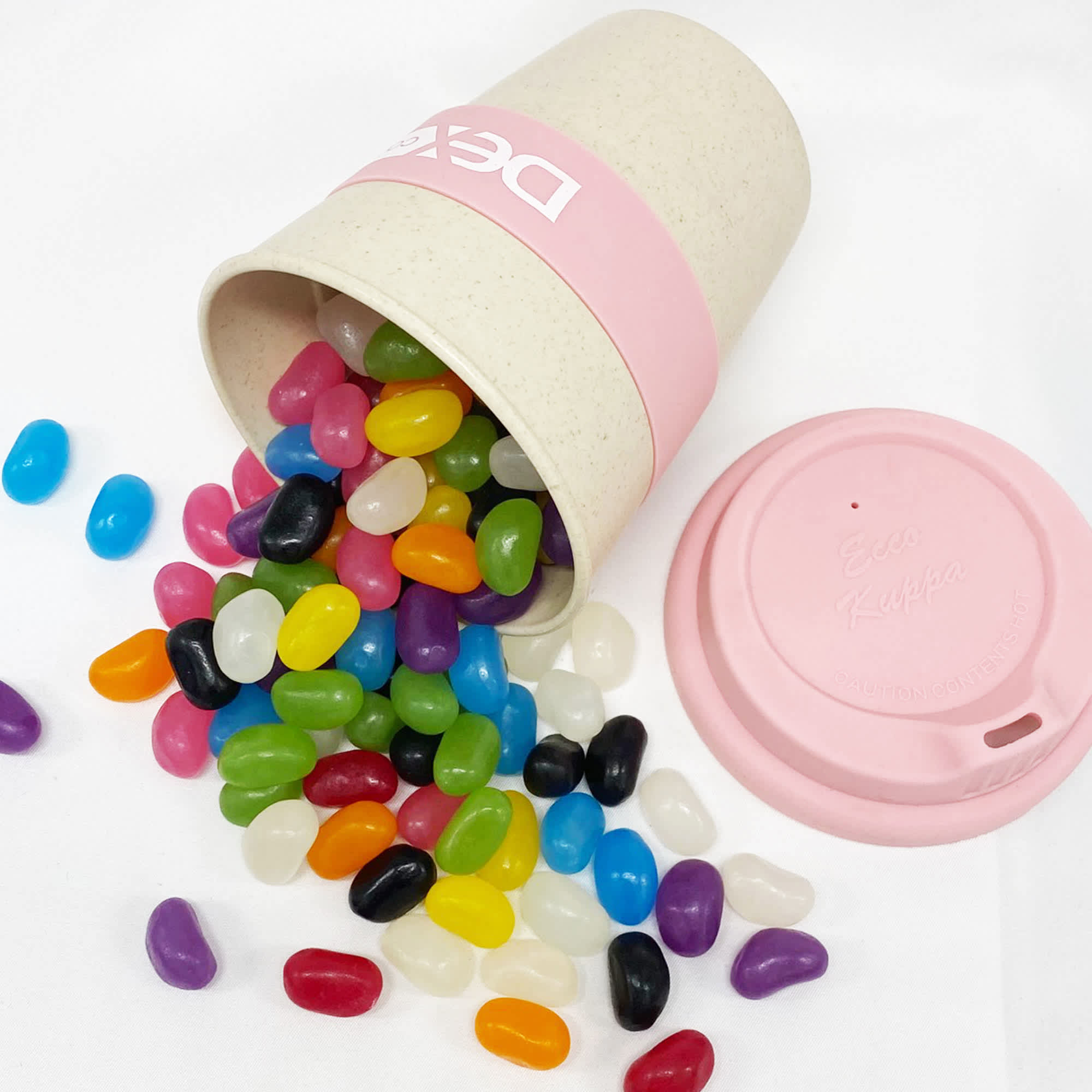 A bamboo cup in pink, spilling an assortment of colourful jelly beans in various shades on a white background. Jelly Bean In 8oz Bamboo Cup - Image 1