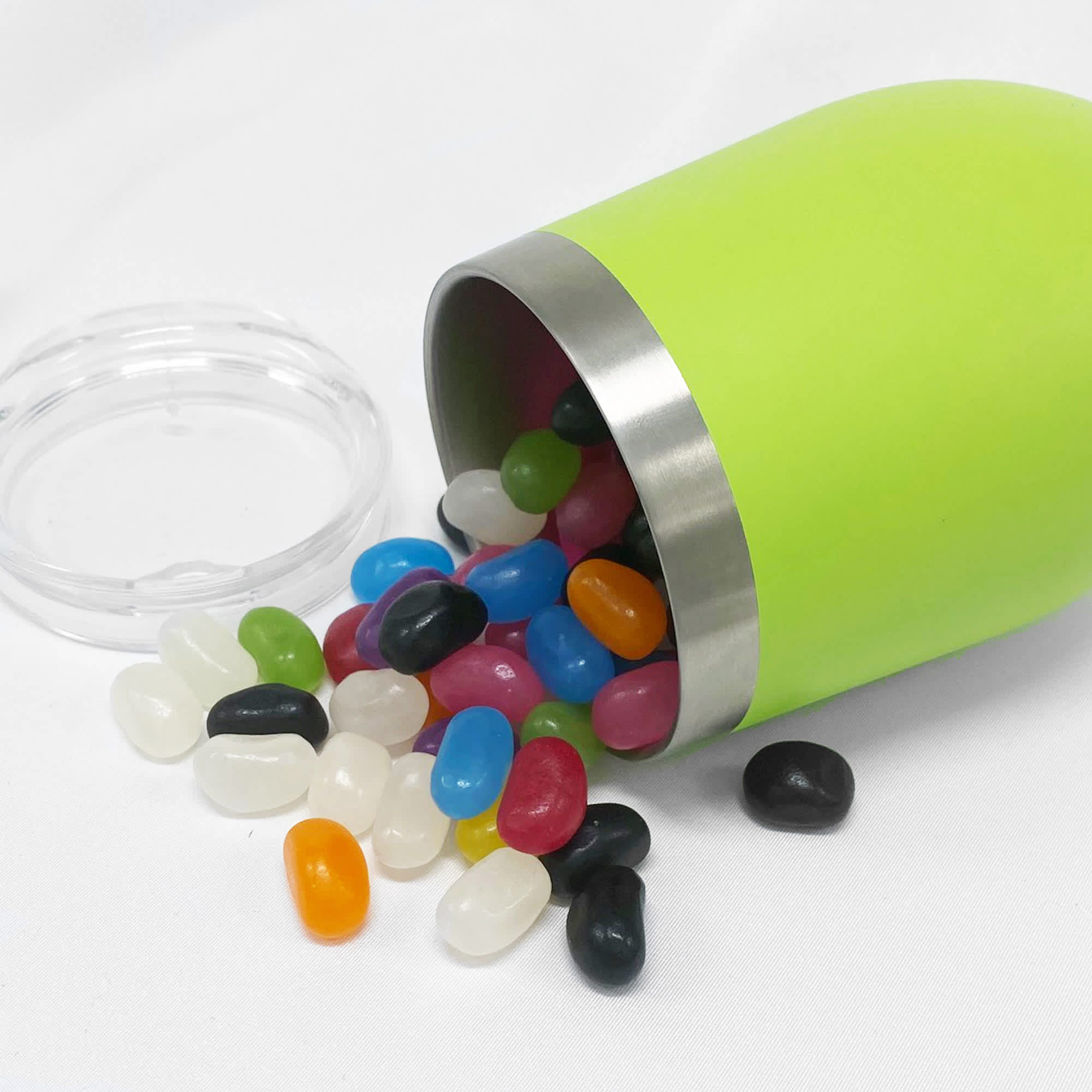 A green coffee mug with a silver rim, filled with colourful jelly beans, tipped over on a white surface. Jelly Bean In Wine Coffee Cup - Image 1