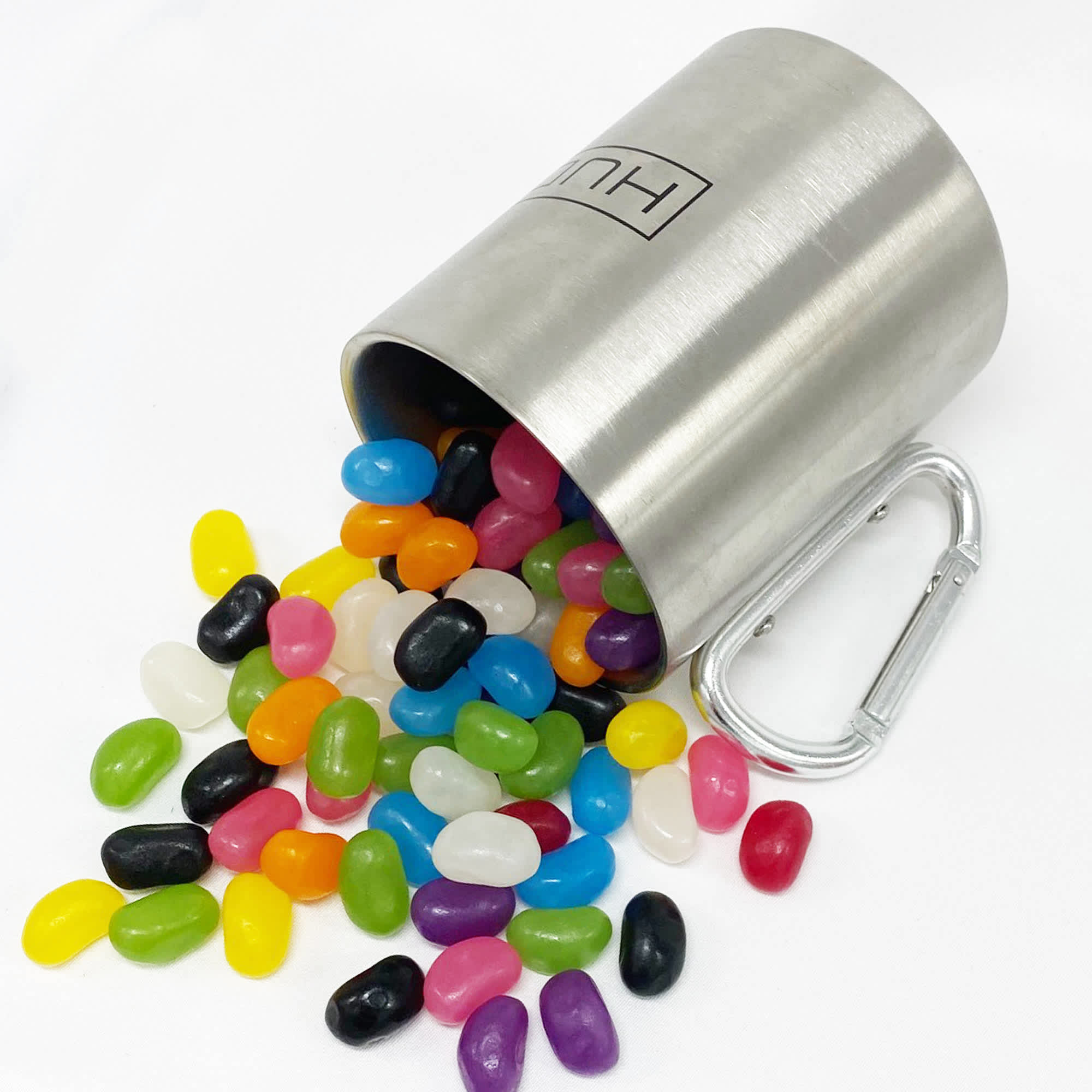 A stainless steel mug spills colourful jelly beans, including shades of yellow, pink, green, black, and white, with a carabiner. Jelly Bean In Bravo Mug - Image 1