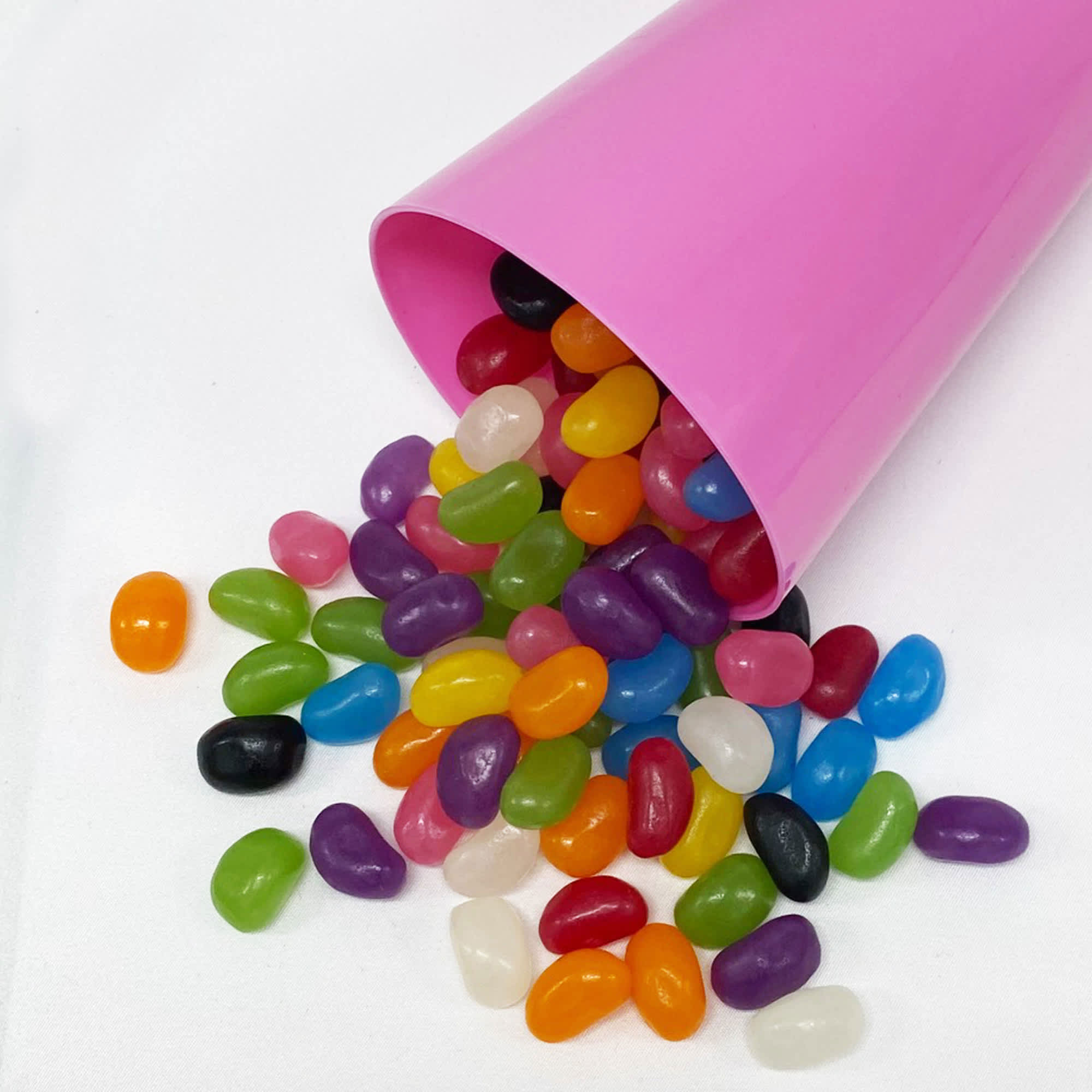 A pink party cup tipped over, spilling a variety of colourful jelly beans in numerous shapes and sizes. Jelly Bean In Party Cup - Image 1