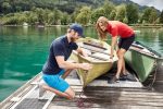 A pair of women’s trekking shorts in black, displayed near boats on a dock by a lake with greenery in the background.