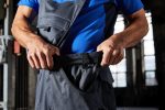 Workwear pants with bib in dark grey, featuring pockets and adjustable straps, being worn by a person.