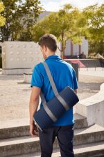 A picnic blanket in a navy blue carry bag is slung over the shoulder of a person wearing a blue shirt.