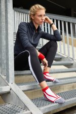 A pair of red and grey sneaker socks worn by a woman sitting on metal stairs, dressed in athletic wear.
