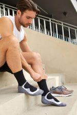 Black sport socks with a grey and white design, worn by a man sitting on steps beside running shoes.