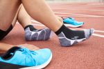 Sport sneaker socks in black and grey, paired with blue athletic shoes, displayed on a track surface.